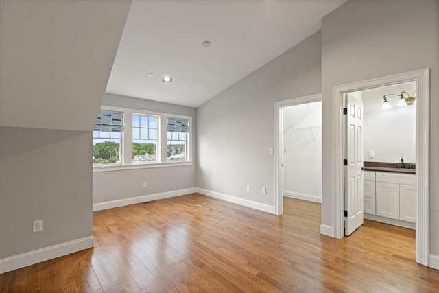 interior space with vaulted ceiling, ensuite bath, light wood-type flooring, a spacious closet, and sink