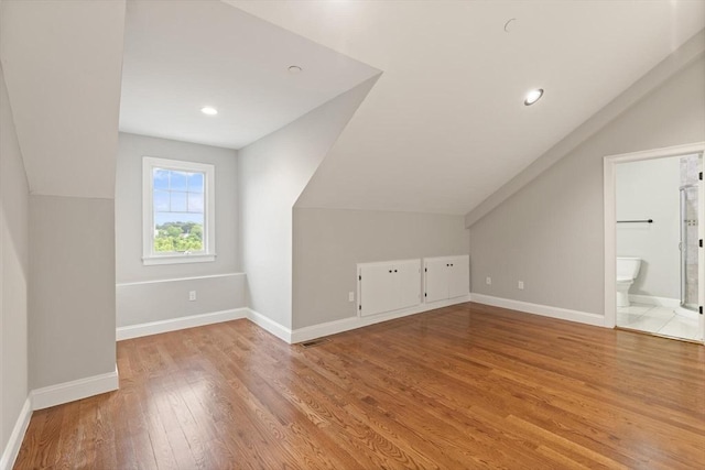 bonus room with light wood-type flooring and vaulted ceiling