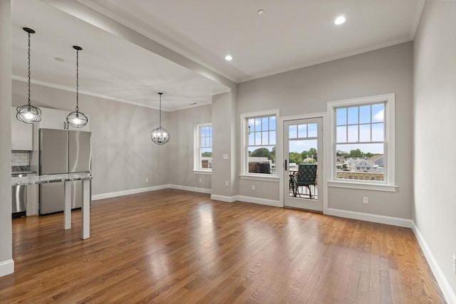 unfurnished living room featuring a healthy amount of sunlight, crown molding, a chandelier, and wood-type flooring