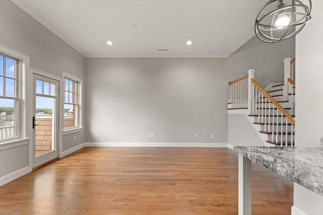 unfurnished living room with a chandelier, light hardwood / wood-style floors, and crown molding