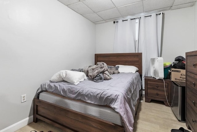 bedroom featuring light wood-type flooring, baseboards, and a drop ceiling