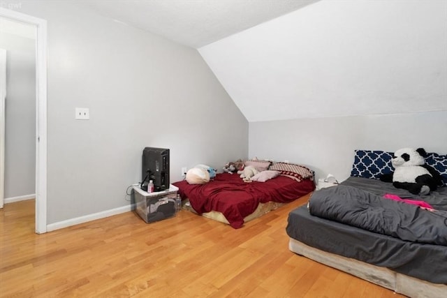 bedroom with baseboards, vaulted ceiling, and wood finished floors