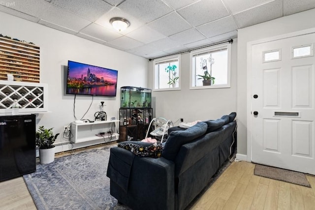 living area with a paneled ceiling, light wood-type flooring, and baseboards