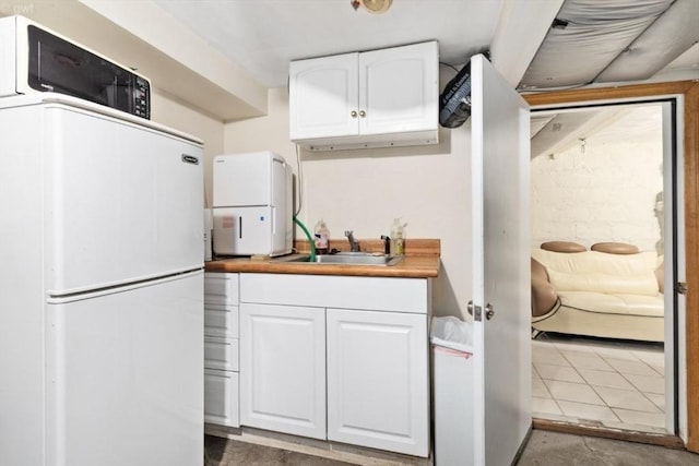 kitchen with light countertops, freestanding refrigerator, a sink, and white cabinets