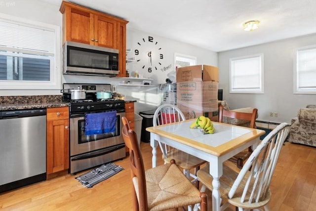 kitchen with stainless steel appliances, light wood-style flooring, brown cabinetry, and dark stone countertops