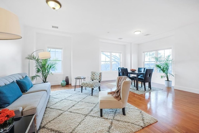 living room featuring a wealth of natural light, visible vents, baseboards, and wood finished floors