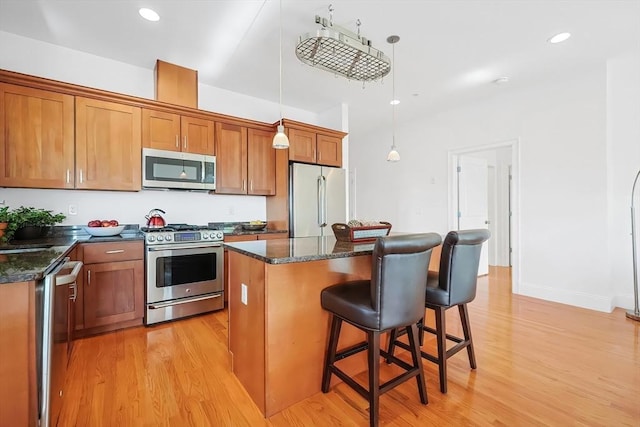 kitchen with a kitchen island, light wood-style flooring, stainless steel appliances, a kitchen bar, and brown cabinets