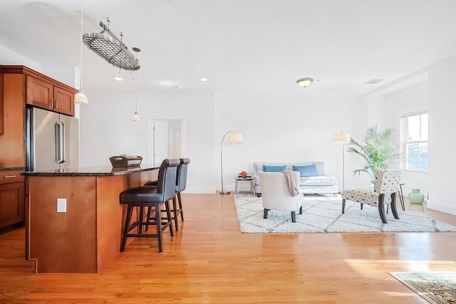 kitchen with brown cabinetry, high end fridge, light wood-style floors, a kitchen breakfast bar, and a center island