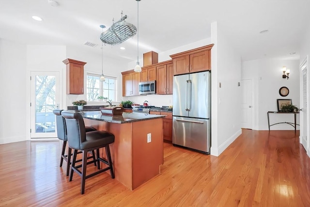 kitchen with a center island, a kitchen bar, light wood-type flooring, brown cabinets, and stainless steel appliances