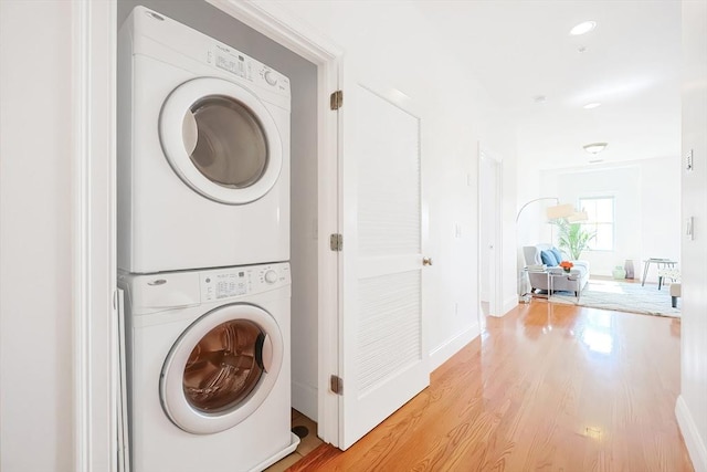 laundry room featuring laundry area, baseboards, stacked washer / drying machine, and light wood-style floors