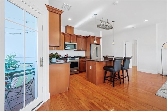 kitchen featuring brown cabinetry, visible vents, light wood-style flooring, stainless steel appliances, and a kitchen bar