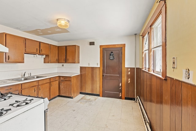 kitchen with a wainscoted wall, light floors, white gas range, light countertops, and wood walls