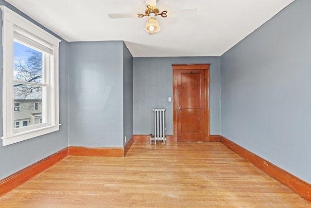 unfurnished room featuring radiator, light wood-style flooring, baseboards, and ceiling fan