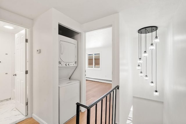 clothes washing area with baseboards, stacked washer and dryer, baseboard heating, and laundry area