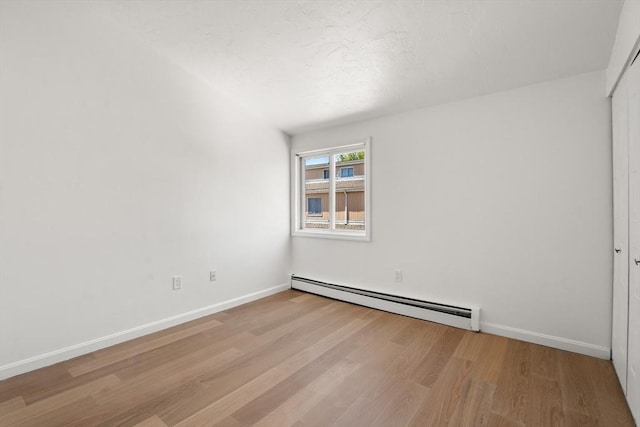 unfurnished bedroom with wood finished floors, baseboards, and a baseboard heating unit