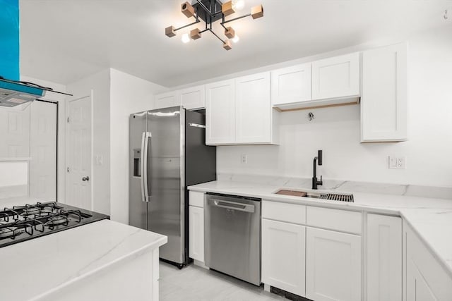 kitchen with wall chimney exhaust hood, white cabinets, appliances with stainless steel finishes, and a sink