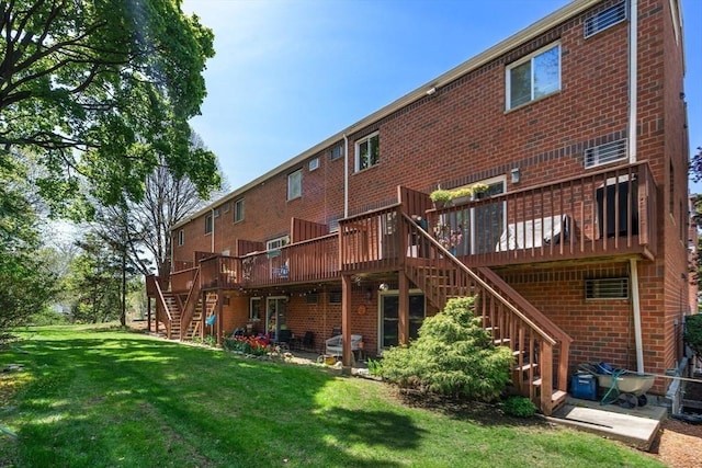 back of property featuring a yard, brick siding, a wooden deck, and stairs