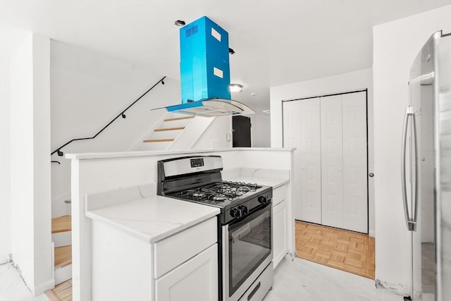kitchen featuring freestanding refrigerator, stainless steel gas range oven, island range hood, white cabinetry, and light stone countertops
