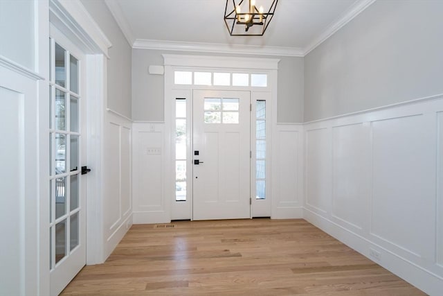 foyer with crown molding, light wood-type flooring, and a chandelier