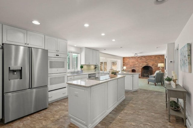 kitchen with stainless steel appliances, a center island, white cabinets, a brick fireplace, and kitchen peninsula