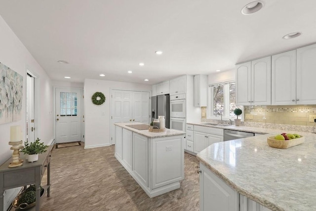 kitchen featuring sink, appliances with stainless steel finishes, white cabinetry, a center island, and light stone counters