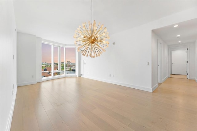 empty room with baseboards, light wood-style floors, and a notable chandelier