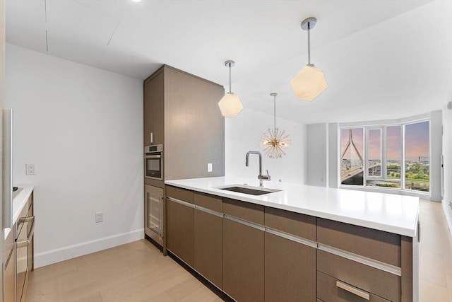 kitchen with a peninsula, a sink, stainless steel oven, light countertops, and light wood-type flooring