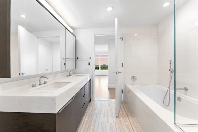 bathroom with a garden tub, double vanity, a sink, and recessed lighting