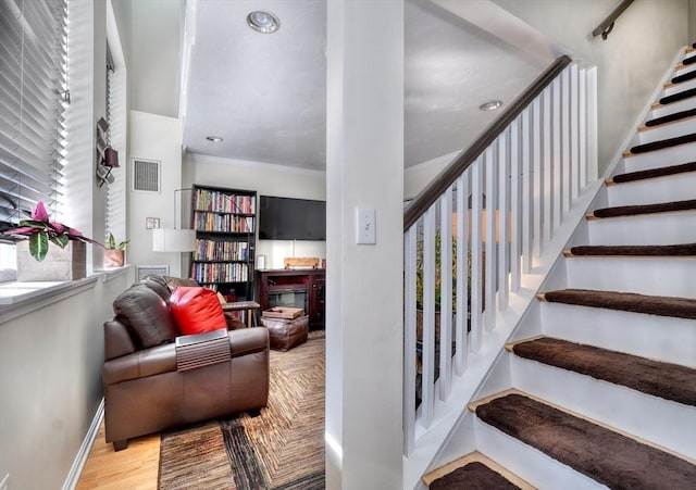 staircase with wood-type flooring and ornamental molding