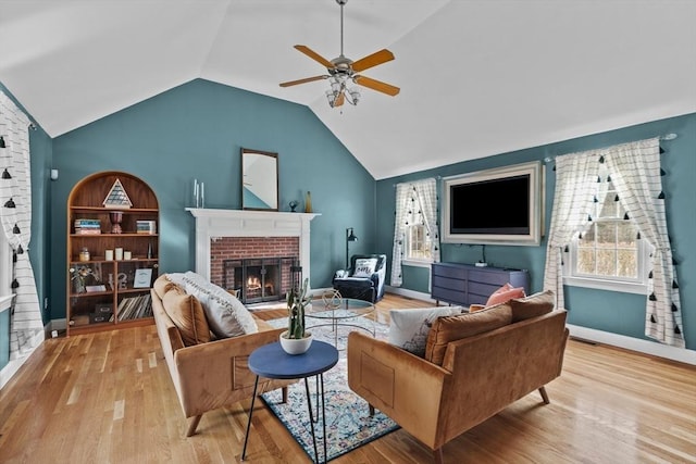 living room with a ceiling fan, wood finished floors, baseboards, a brick fireplace, and vaulted ceiling