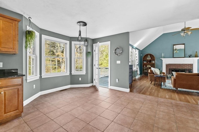 dining space with ceiling fan, baseboards, vaulted ceiling, a fireplace, and light tile patterned flooring