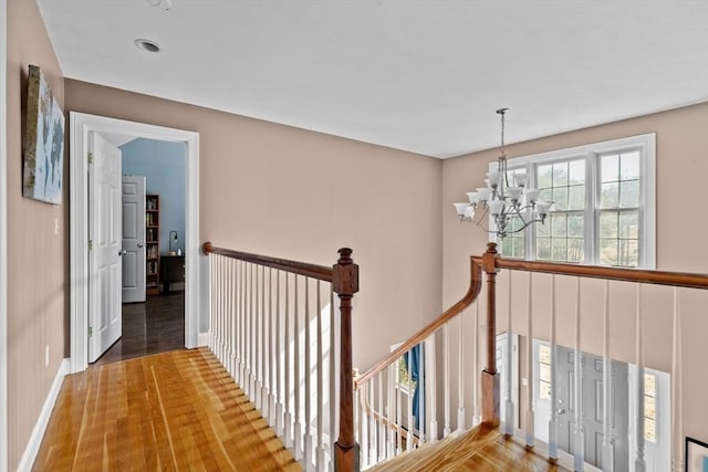 hall featuring an inviting chandelier, wood finished floors, an upstairs landing, and baseboards