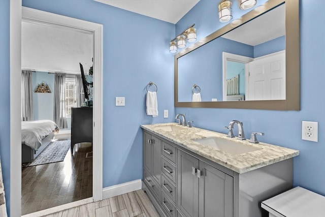 ensuite bathroom with ensuite bath, wood finished floors, baseboards, and a sink