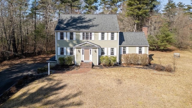 colonial inspired home with a chimney, driveway, and a shingled roof