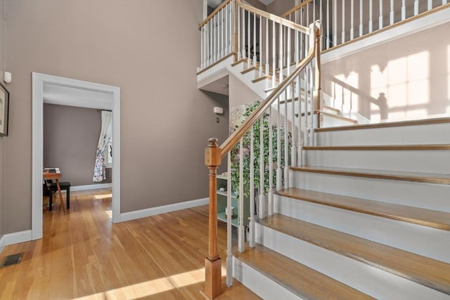 stairway featuring visible vents, a high ceiling, baseboards, and wood finished floors