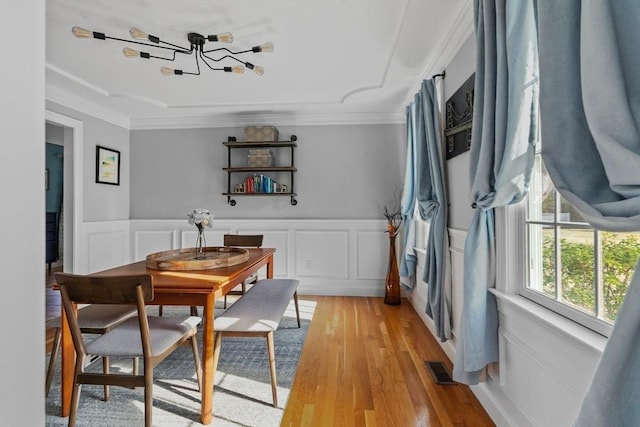 dining space with light wood finished floors, visible vents, crown molding, and a wainscoted wall