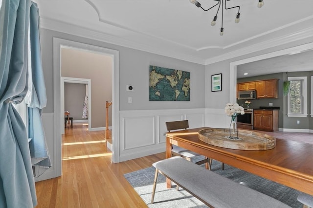 dining area with a wainscoted wall, light wood-style flooring, a decorative wall, and ornamental molding