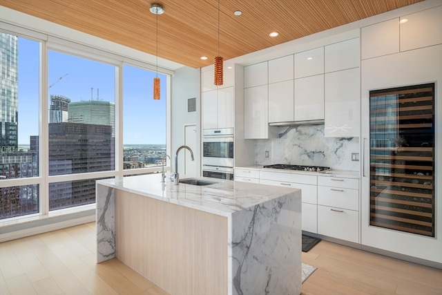 kitchen featuring pendant lighting, sink, beverage cooler, white cabinets, and light hardwood / wood-style flooring