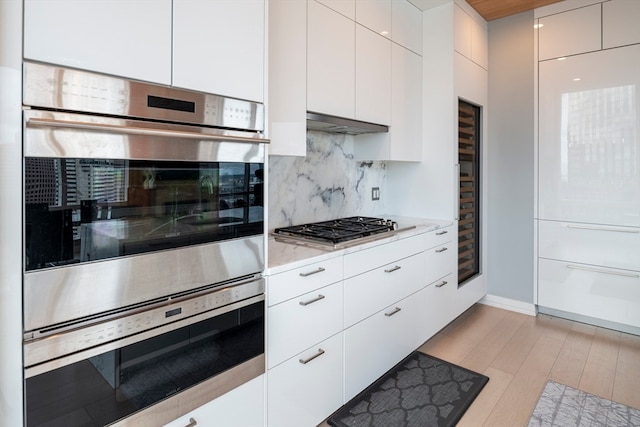 kitchen featuring light hardwood / wood-style flooring, white cabinetry, ventilation hood, appliances with stainless steel finishes, and decorative backsplash