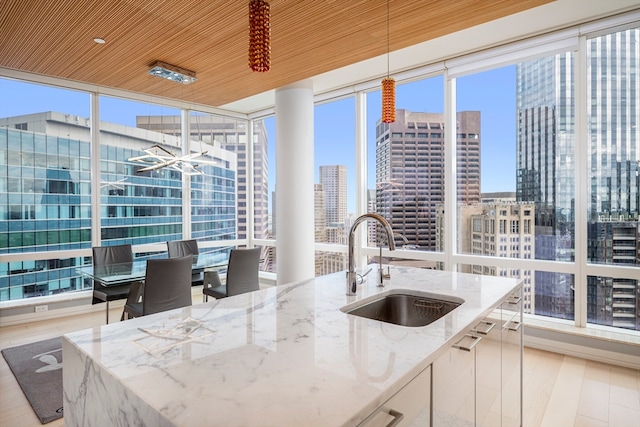 kitchen with pendant lighting, light stone countertops, white cabinets, sink, and light wood-type flooring