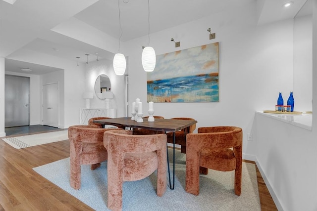 dining area featuring a tray ceiling, wood finished floors, and baseboards