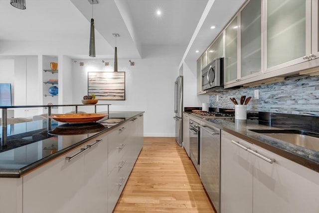 kitchen featuring dark stone counters, glass insert cabinets, stainless steel appliances, light wood-style floors, and backsplash