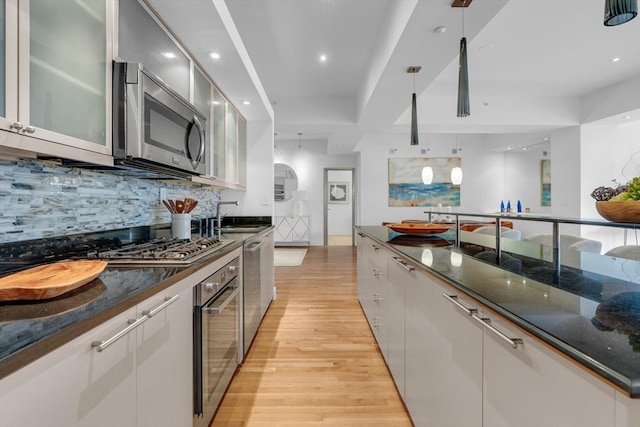 kitchen with light wood-style flooring, glass insert cabinets, stainless steel appliances, white cabinetry, and backsplash