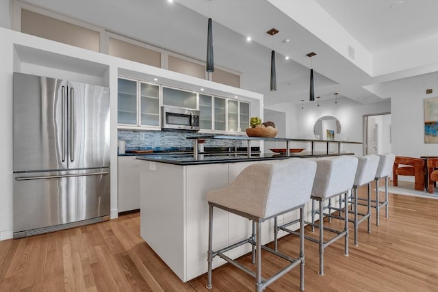 kitchen featuring light wood finished floors, tasteful backsplash, white cabinets, dark countertops, and stainless steel appliances