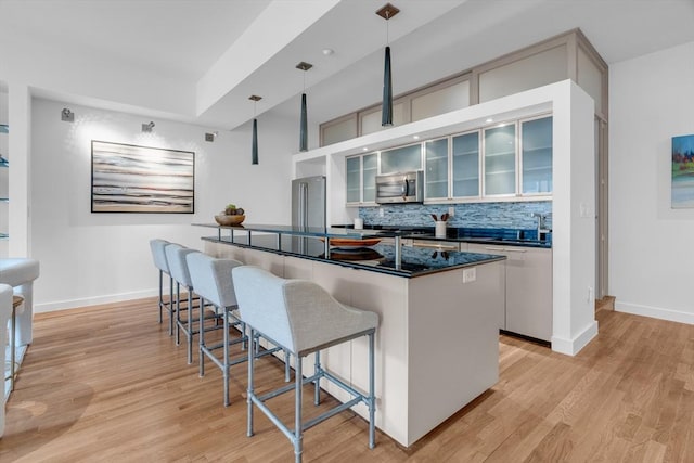 kitchen featuring dark countertops, light wood-style flooring, stainless steel microwave, a kitchen bar, and a sink