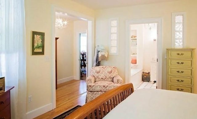 bedroom featuring an inviting chandelier, ensuite bathroom, baseboards, and wood finished floors