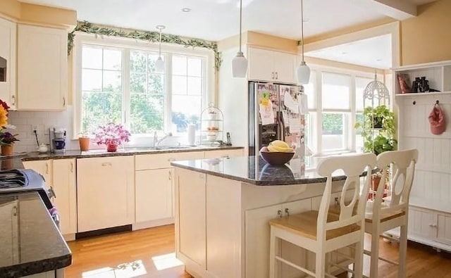 kitchen with a sink, dark stone counters, stainless steel fridge, and light wood-style floors