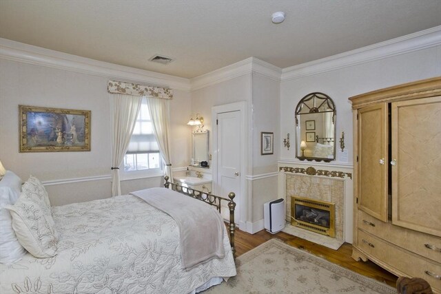bedroom featuring a premium fireplace, visible vents, crown molding, and wood finished floors