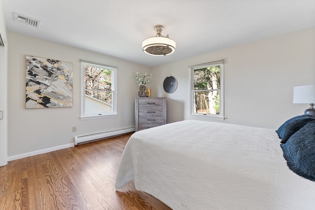 bedroom with hardwood / wood-style flooring, a baseboard radiator, and multiple windows