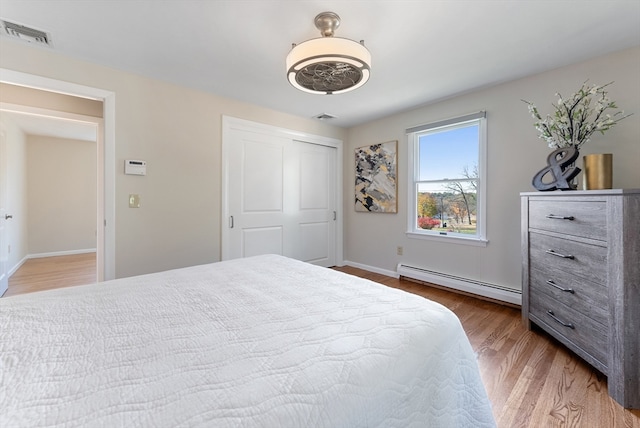 bedroom featuring a baseboard heating unit, hardwood / wood-style floors, and a closet